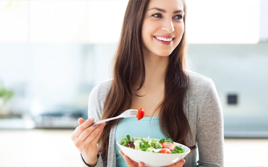 A person is holding a bowl of fresh salad and lifting a fork
